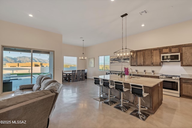 kitchen with a notable chandelier, a kitchen breakfast bar, stainless steel range with gas cooktop, visible vents, and a sink