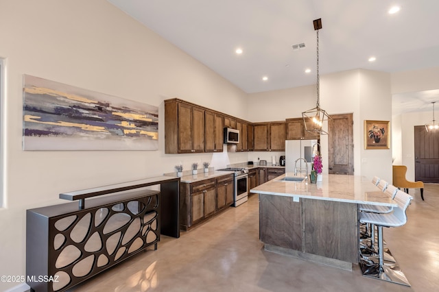 kitchen with a kitchen breakfast bar, light stone countertops, appliances with stainless steel finishes, finished concrete floors, and a sink