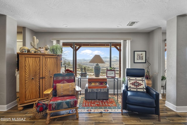 sitting room with wood finish floors, a textured wall, baseboards, and visible vents