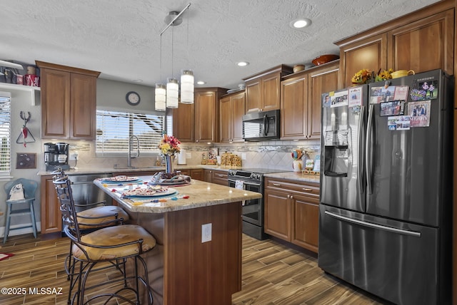 kitchen featuring wood tiled floor, a sink, a kitchen bar, and appliances with stainless steel finishes