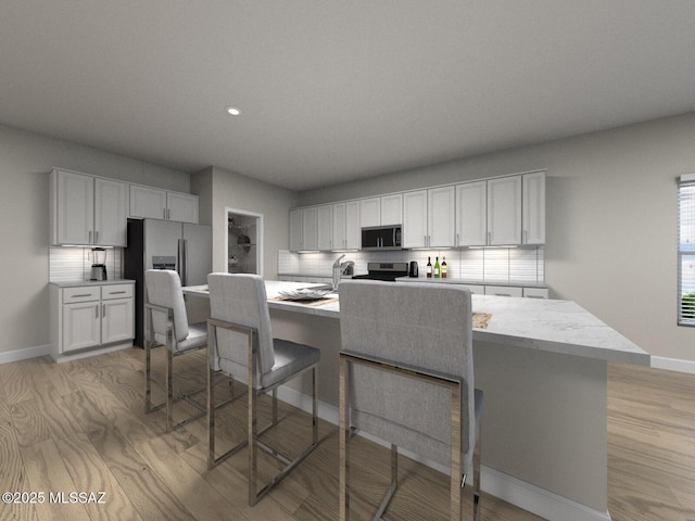 kitchen featuring tasteful backsplash, a kitchen island with sink, stainless steel appliances, light wood-style flooring, and a breakfast bar area