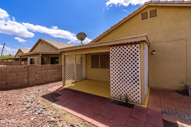 exterior space with stucco siding, a tile roof, fence, and a patio area