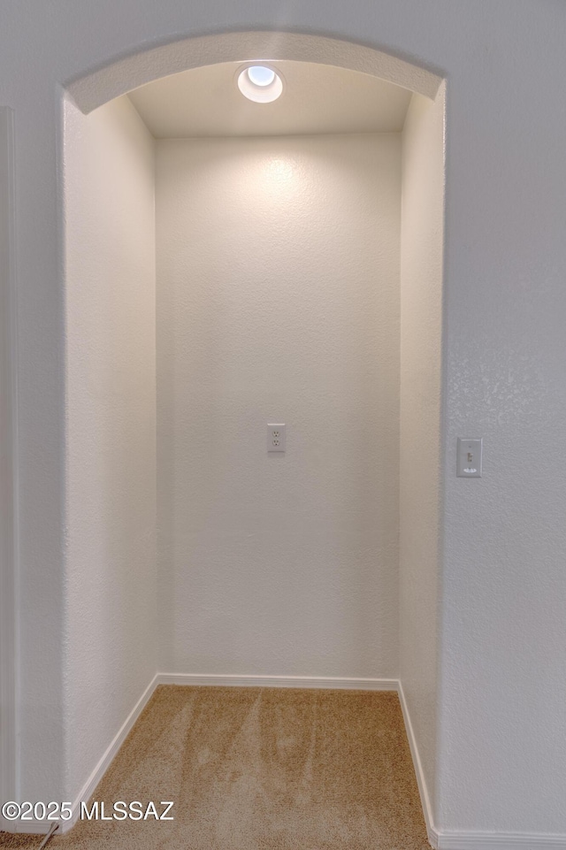 interior space with arched walkways, baseboards, and light carpet