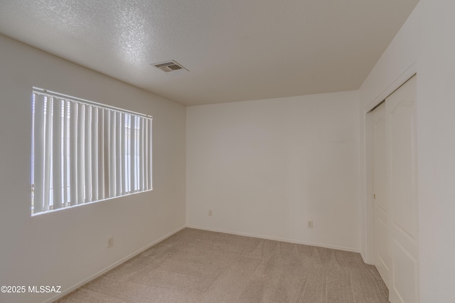 spare room with light carpet, baseboards, visible vents, and a textured ceiling