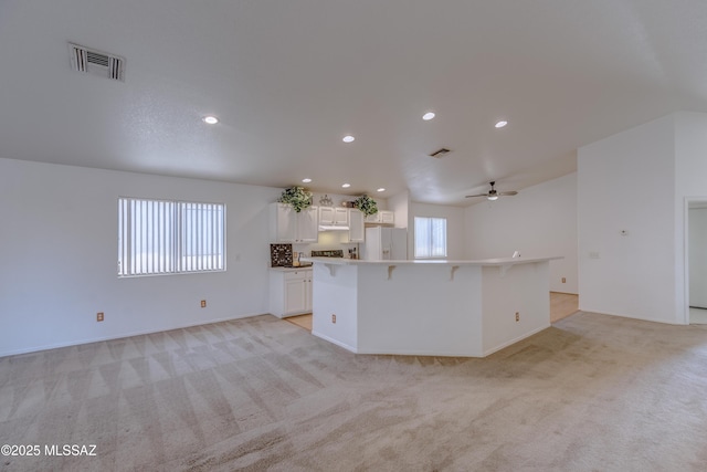 kitchen with white cabinets, visible vents, white refrigerator with ice dispenser, and light colored carpet