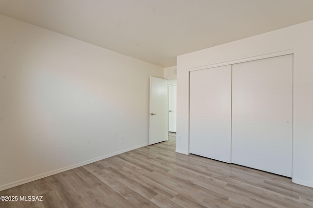 unfurnished bedroom with light wood-style flooring, a closet, and baseboards