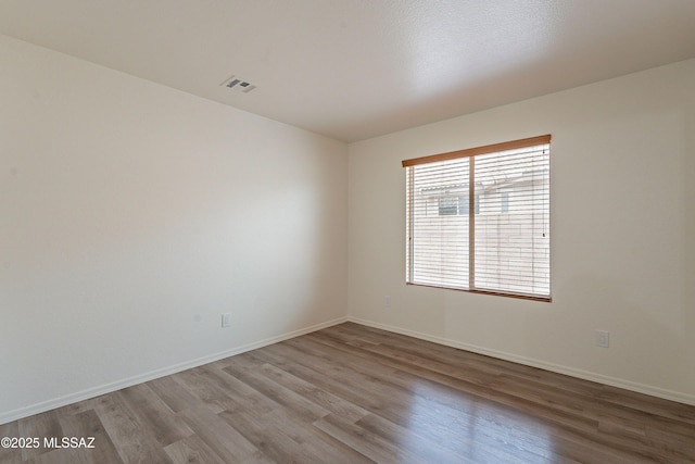 empty room featuring baseboards, visible vents, and wood finished floors