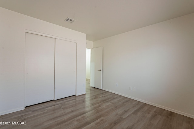 unfurnished bedroom with visible vents, baseboards, a closet, and wood finished floors