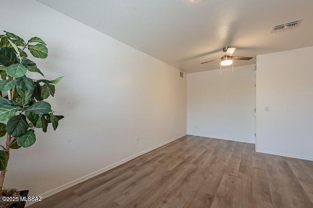 spare room featuring wood finished floors, baseboards, ceiling fan, and visible vents