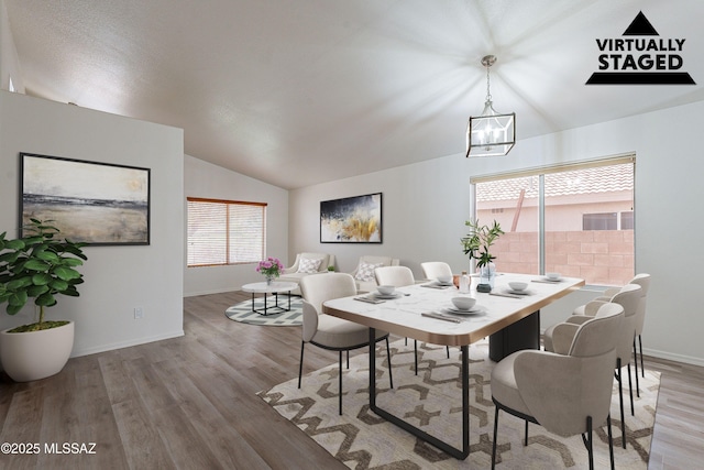 dining area featuring light wood-style flooring, a notable chandelier, baseboards, and vaulted ceiling