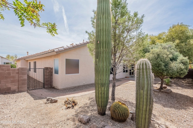 view of home's exterior featuring a gate, fence, a patio, a tile roof, and stucco siding