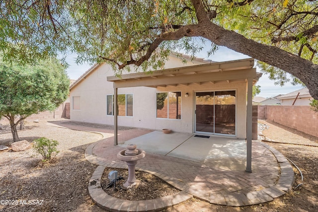 rear view of house featuring stucco siding, fence, and a patio area
