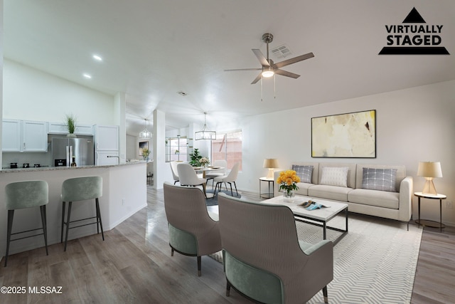 living area featuring vaulted ceiling, baseboards, light wood finished floors, visible vents, and a ceiling fan