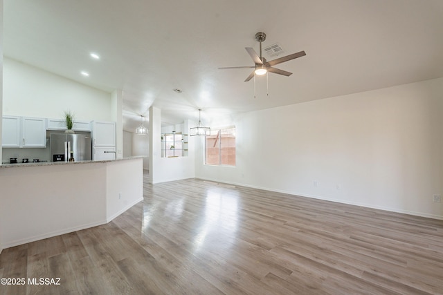 unfurnished living room featuring vaulted ceiling, light wood finished floors, baseboards, ceiling fan with notable chandelier, and visible vents