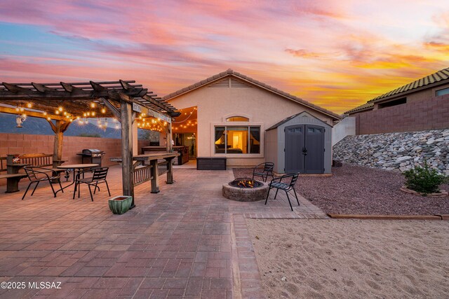61080 Halter Pl, Saddlebrooke, AZ 85739 - patio terrace at dusk featuring an outbuilding, fence, an outdoor fire pit, a pergola, and a storage shed