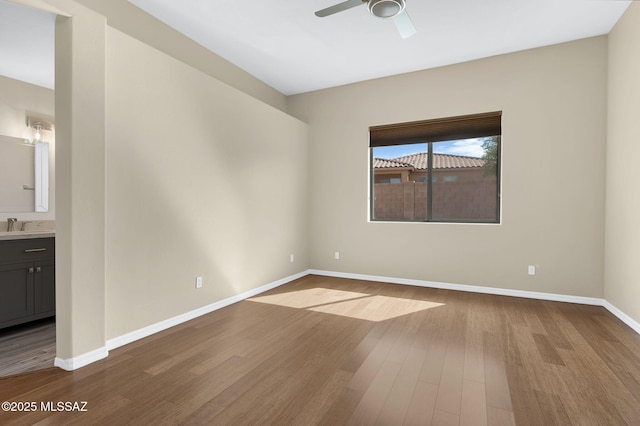 spare room featuring a ceiling fan, baseboards, a sink, and dark wood finished floors