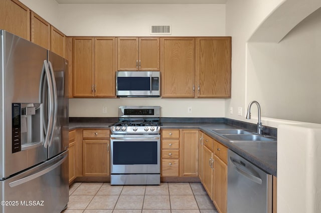kitchen featuring stainless steel appliances, dark countertops, visible vents, light tile patterned floors, and a sink