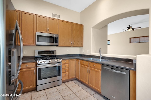 kitchen with dark countertops, a ceiling fan, stainless steel appliances, and a sink