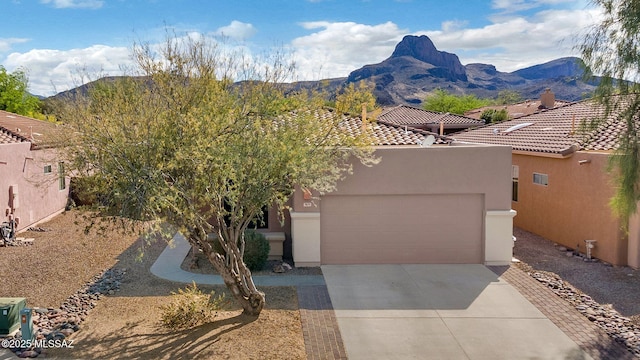 view of front facade with stucco siding, an attached garage, a mountain view, and driveway