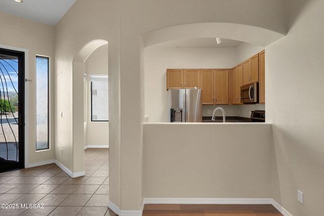 kitchen with tile patterned floors, a sink, arched walkways, baseboards, and appliances with stainless steel finishes