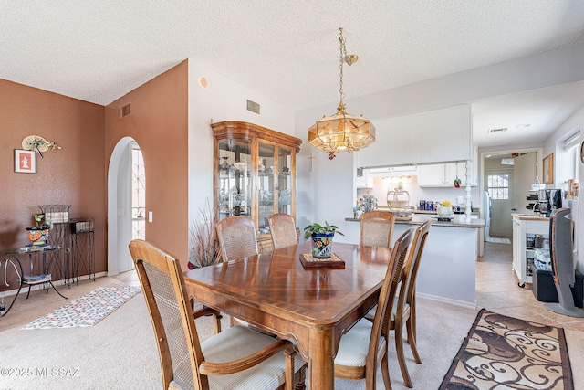 dining area with light carpet, a notable chandelier, arched walkways, and visible vents