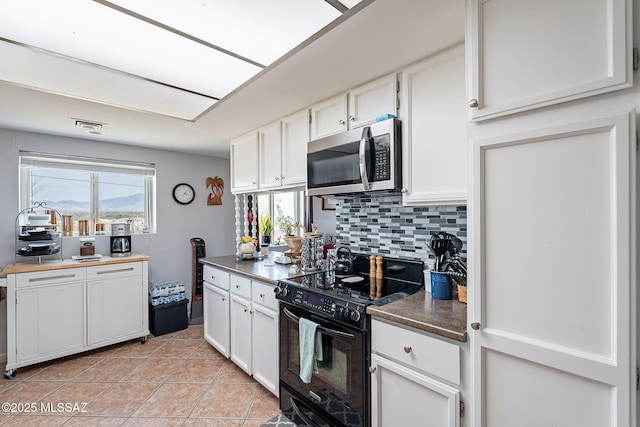 kitchen with white cabinetry, light tile patterned floors, stainless steel microwave, decorative backsplash, and black / electric stove