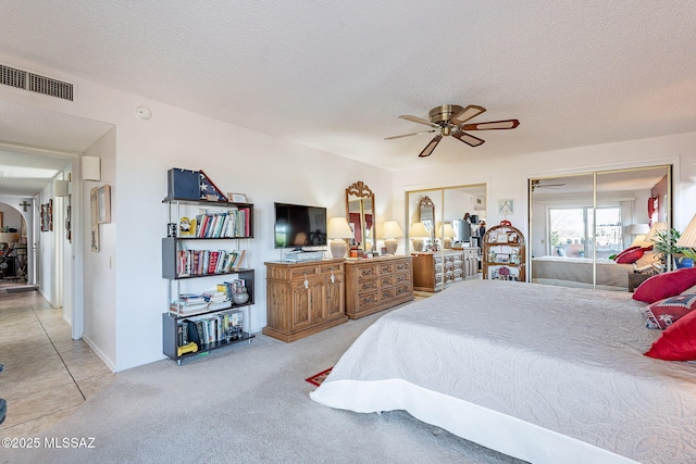 bedroom featuring multiple closets, a textured ceiling, visible vents, a ceiling fan, and light carpet