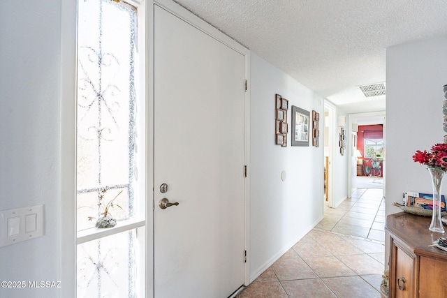 hall featuring light tile patterned flooring, a textured ceiling, and visible vents