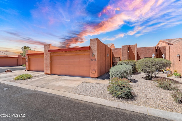 pueblo-style house with an attached garage, driveway, and stucco siding