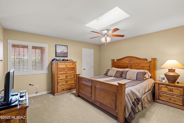 bedroom featuring light colored carpet, a ceiling fan, baseboards, and a skylight