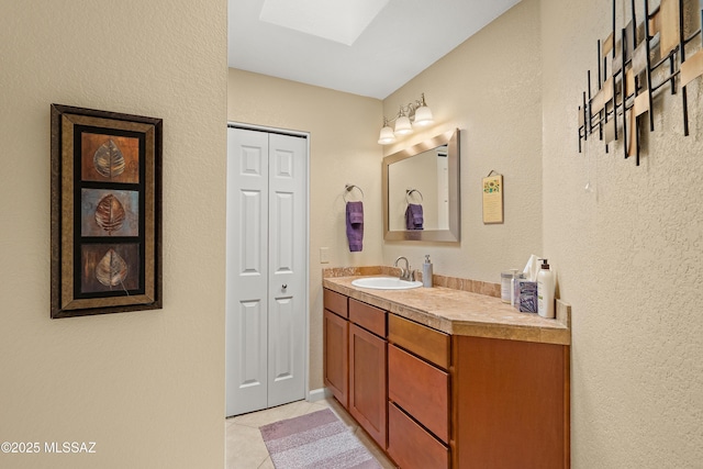 bathroom featuring a textured wall, vanity, tile patterned floors, a skylight, and a closet