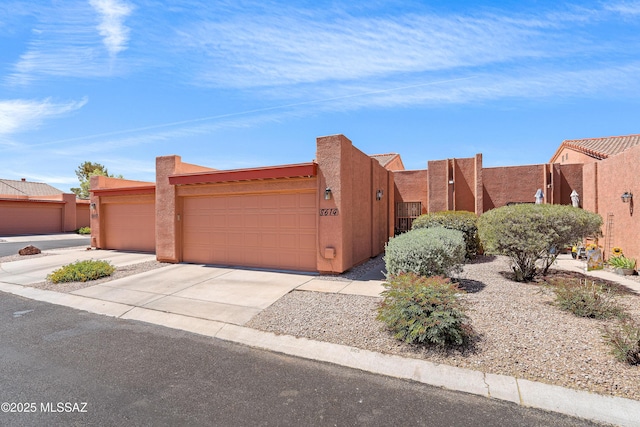 pueblo-style house with a garage, stucco siding, and concrete driveway