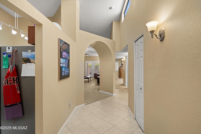 hallway with a textured wall, light tile patterned flooring, baseboards, a high ceiling, and arched walkways