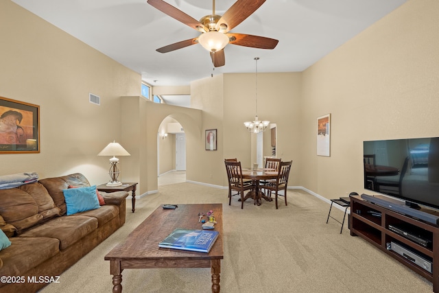 living room featuring visible vents, a towering ceiling, light colored carpet, arched walkways, and ceiling fan with notable chandelier