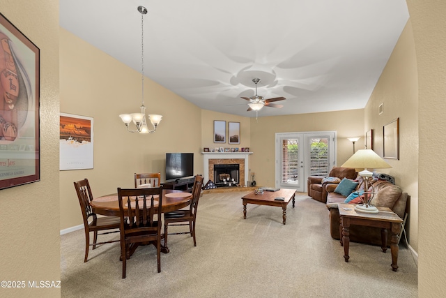 dining room with a fireplace with raised hearth, baseboards, light colored carpet, and ceiling fan with notable chandelier