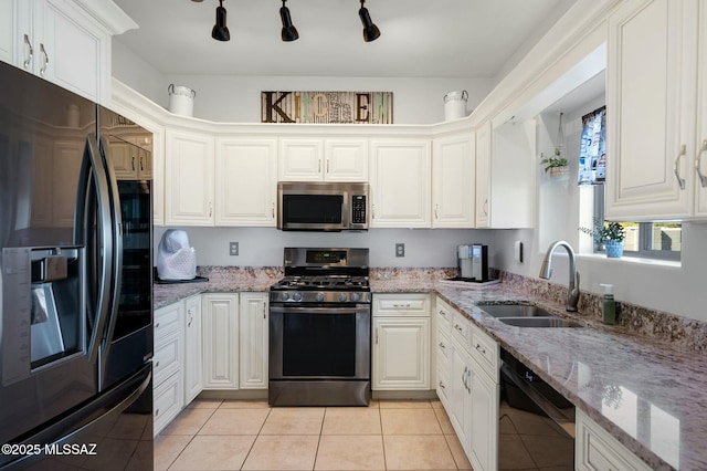 kitchen featuring appliances with stainless steel finishes, light stone counters, a sink, white cabinetry, and light tile patterned floors
