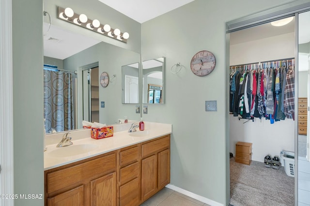 bathroom featuring visible vents, double vanity, baseboards, a spacious closet, and a sink