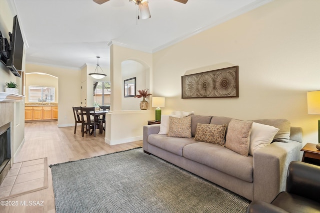 7050 E Sunrise Dr Unit 1104, Tucson, AZ 85750 - living room with arched walkways, crown molding, light wood-style floors, a tile fireplace, and a ceiling fan