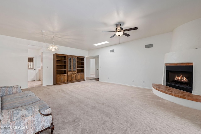 unfurnished living room featuring a brick fireplace, light carpet, ceiling fan with notable chandelier, and visible vents