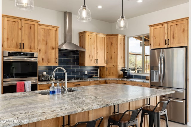 kitchen with wall chimney exhaust hood, a kitchen bar, appliances with stainless steel finishes, a sink, and backsplash