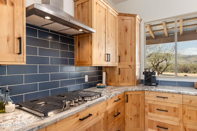 kitchen featuring tasteful backsplash, light brown cabinets, light stone counters, wall chimney range hood, and stainless steel gas stovetop