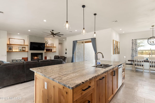 kitchen with recessed lighting, a ceiling fan, light stone countertops, a kitchen island with sink, and a sink