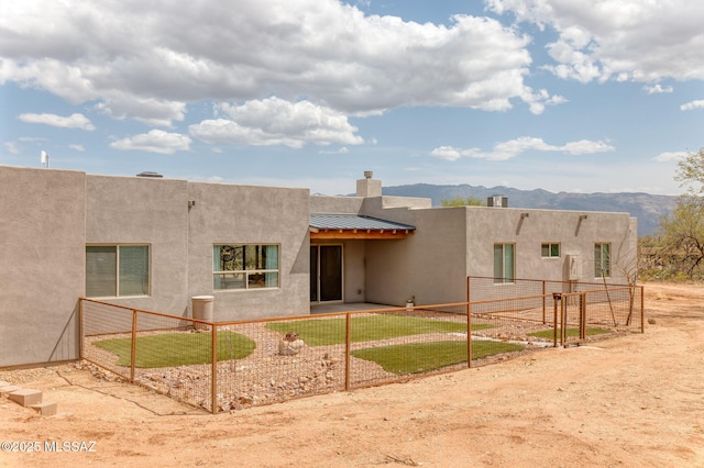 rear view of property with a mountain view, metal roof, stucco siding, and fence