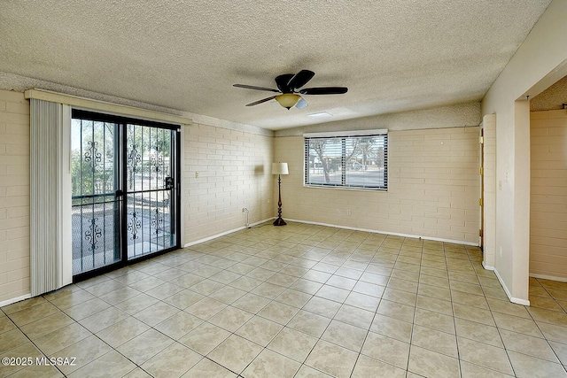 empty room featuring light tile patterned floors, brick wall, and a ceiling fan