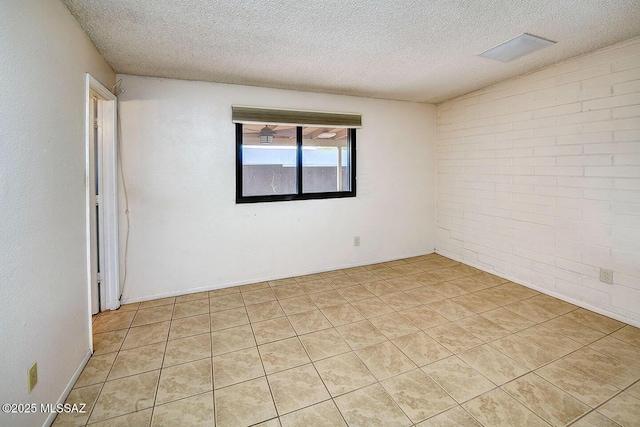 spare room featuring light tile patterned flooring, brick wall, and a textured ceiling