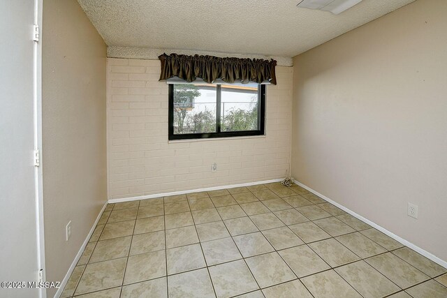 empty room featuring light tile patterned flooring, baseboards, and a textured ceiling