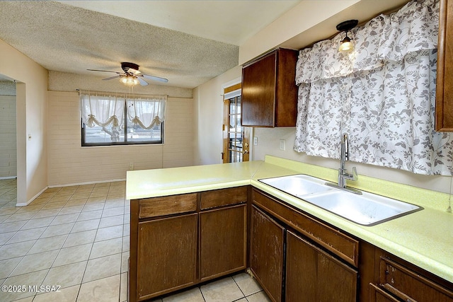 kitchen with light tile patterned flooring, a textured ceiling, a peninsula, a ceiling fan, and a sink