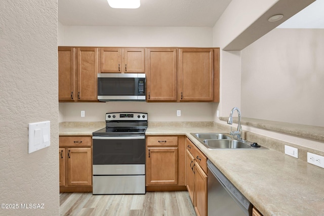 kitchen featuring light countertops, a sink, light wood finished floors, appliances with stainless steel finishes, and a textured wall