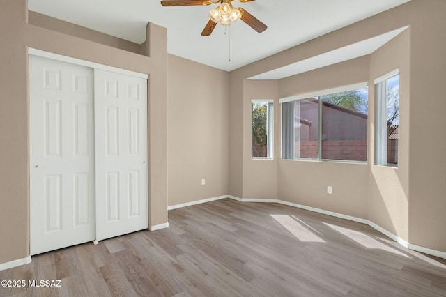 unfurnished bedroom featuring baseboards, wood finished floors, a closet, and a ceiling fan