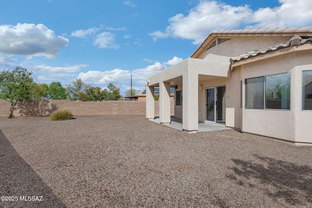 rear view of house with stucco siding, a fenced backyard, a tiled roof, and a patio area